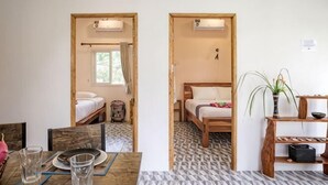 A room with two beds, a dining table with glasses, a plant, and a patterned floor. - Enda Lanta Bungalows (Ko Lanta)