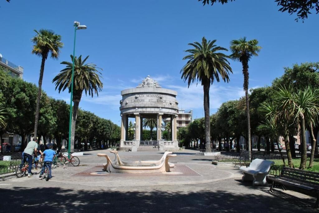 A circular monument with inscriptions, surrounded by palm trees and benches in a park setting.