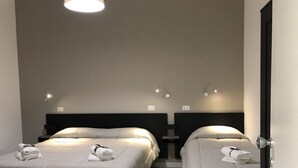 Een hotelkamer met twee bedden, elk voorzien van een kussen en een opgerolde handdoek. Boven elk bed hangen wandlampen.