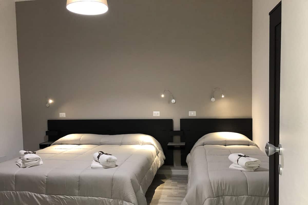 Une chambre d’hôtel avec deux lits, chacun équipé d’un oreiller et d’une serviette enroulée. Des appliques murales sont fixées au-dessus de chaque lit.