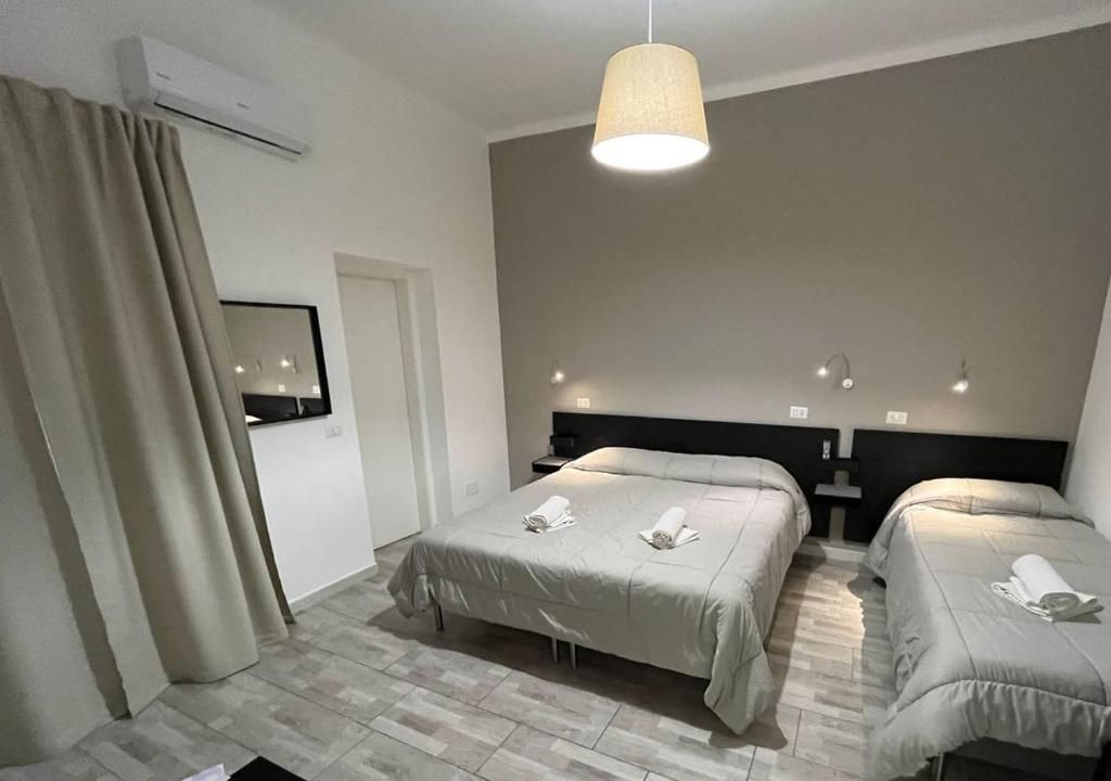 Una camera d'albergo con due letti, un'ampia finestra con tende, una ventola a soffitto e un condizionatore d'aria a parete.