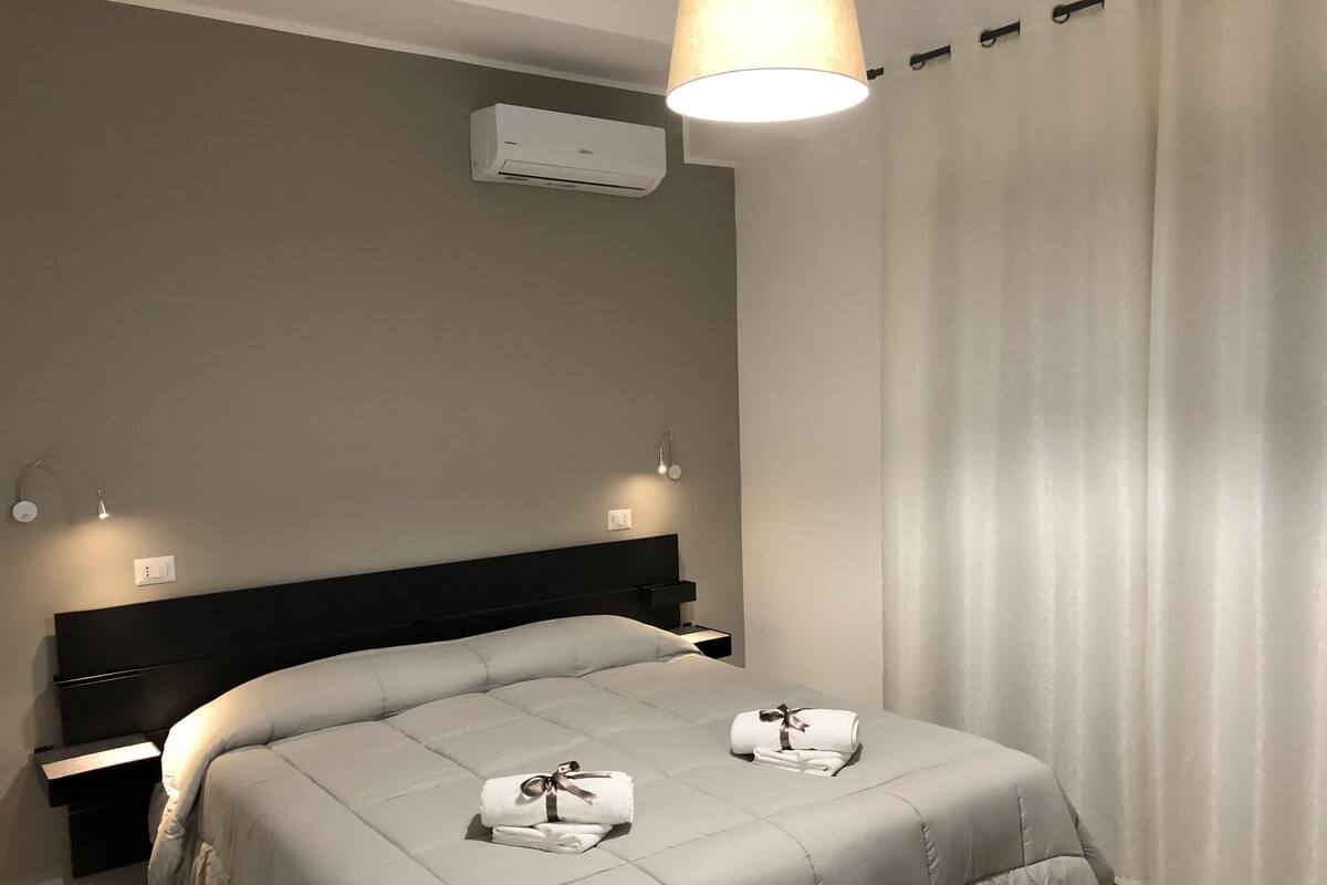 Une chambre d’hôtel équipée d’un lit, de tables de chevet, d’un appareil de climatisation et d’une fenêtre avec des rideaux.