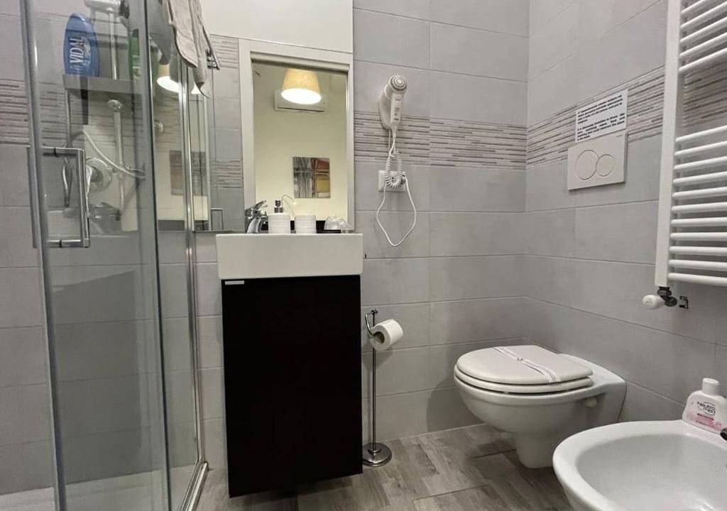 A bathroom with a glass shower enclosure, a toilet, a bidet, and a sink with a mirror.