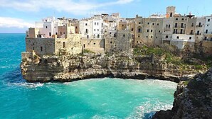 Een kustplaatsje met historische stenen gebouwen op een klif met uitzicht op turquoise water.