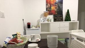 Een eethoek met een tafel gedekt voor twee personen, inclusief een mand met lekkernijen, een koffiemok en een theezakje.