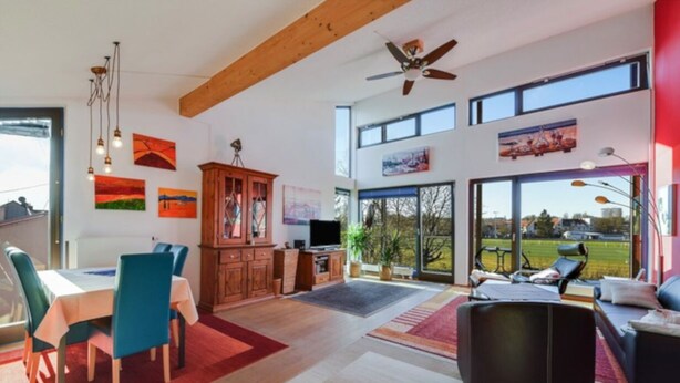 A spacious living area with a dining table, chairs, a sofa, and a large window offering a view of the outdoors.