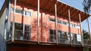 A multi-story building with a red facade, large windows, and a balcony with metal railings.