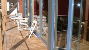 A covered outdoor patio with tables and chairs, large sliding glass doors, and a wooden deck.