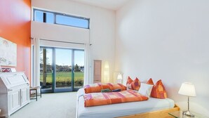 A bedroom with a large bed, a glass table, a desk, and a view of a green landscape through a sliding door.