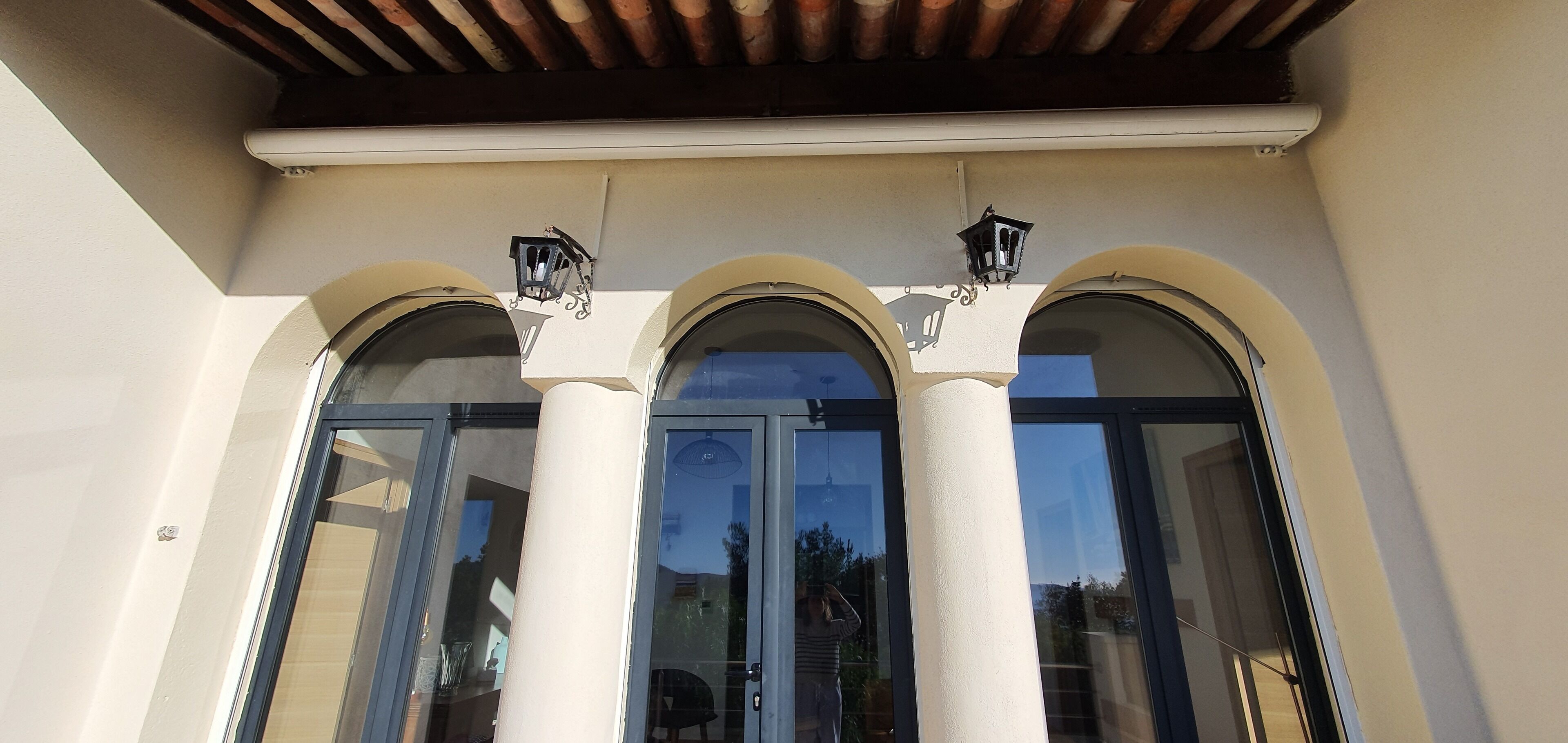 Fachada de edificio con tres ventanales arqueados y dos faroles en la pared.