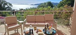 A balcony with a sofa, chairs, and a table with food and drinks.