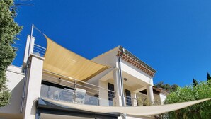A two-story house with a balcony, a sliding glass door leading to an outdoor seating area, and a hammock. - STANDING villa, 450m from the BEACHES, heated SWIMMING POOL, SUPERB SEA VIEW, beautiful garden (Le Lavandou)