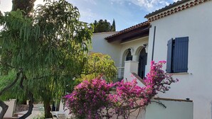 A building with a white facade, a tiled roof, and a window with blue shutters. - STANDING villa, 450m from the BEACHES, heated SWIMMING POOL, SUPERB SEA VIEW, beautiful garden (Le Lavandou)