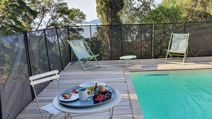 A poolside area with a table set for breakfast, including a tray with food and drinks, two lounge chairs, and a view of the surrounding trees and mountains. - STANDING villa, 450m from the BEACHES, heated SWIMMING POOL, SUPERB SEA VIEW, beautiful garden (Le Lavandou)