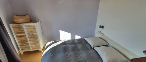 A bedroom with a bed, pillows, a nightstand, a lamp, a wardrobe, and a woven basket on top.