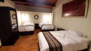 A room with two beds, wooden flooring, a mirror, and a painting on the wall.
