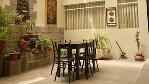 A spacious indoor courtyard with a round table and chairs, surrounded by potted plants and a stone wall.