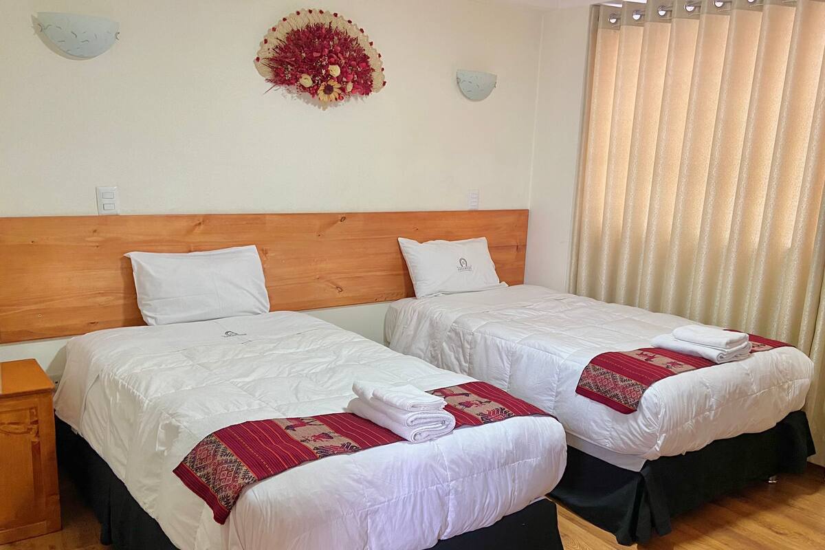 Habitación de hotel con dos camas, cabeceros de madera, ropa de cama blanca y un tapiz decorativo.