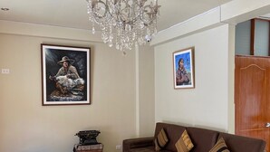 A living room with a brown sofa, a wooden floor, a chandelier, and two framed pictures on the wall.