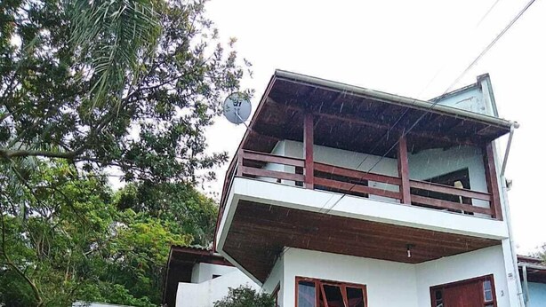 A two-story house with a stone staircase leading to the entrance, surrounded by greenery. - Residencial Rodrigues (Florianópolis)
