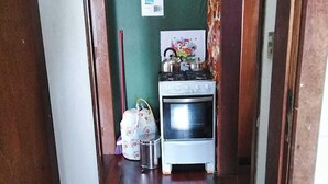 A narrow hallway with a wooden floor, a small kitchenette area with a stove and oven, a trash bin, and a wall-mounted light switch. - Residencial Rodrigues (Florianópolis)