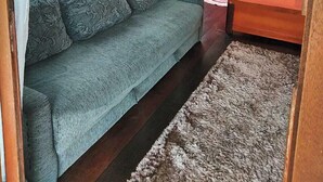 A small, cozy room with a grey sofa, a bed with an orange blanket, a wooden door, and a framed picture on the wall. - Residencial Rodrigues (Florianópolis)