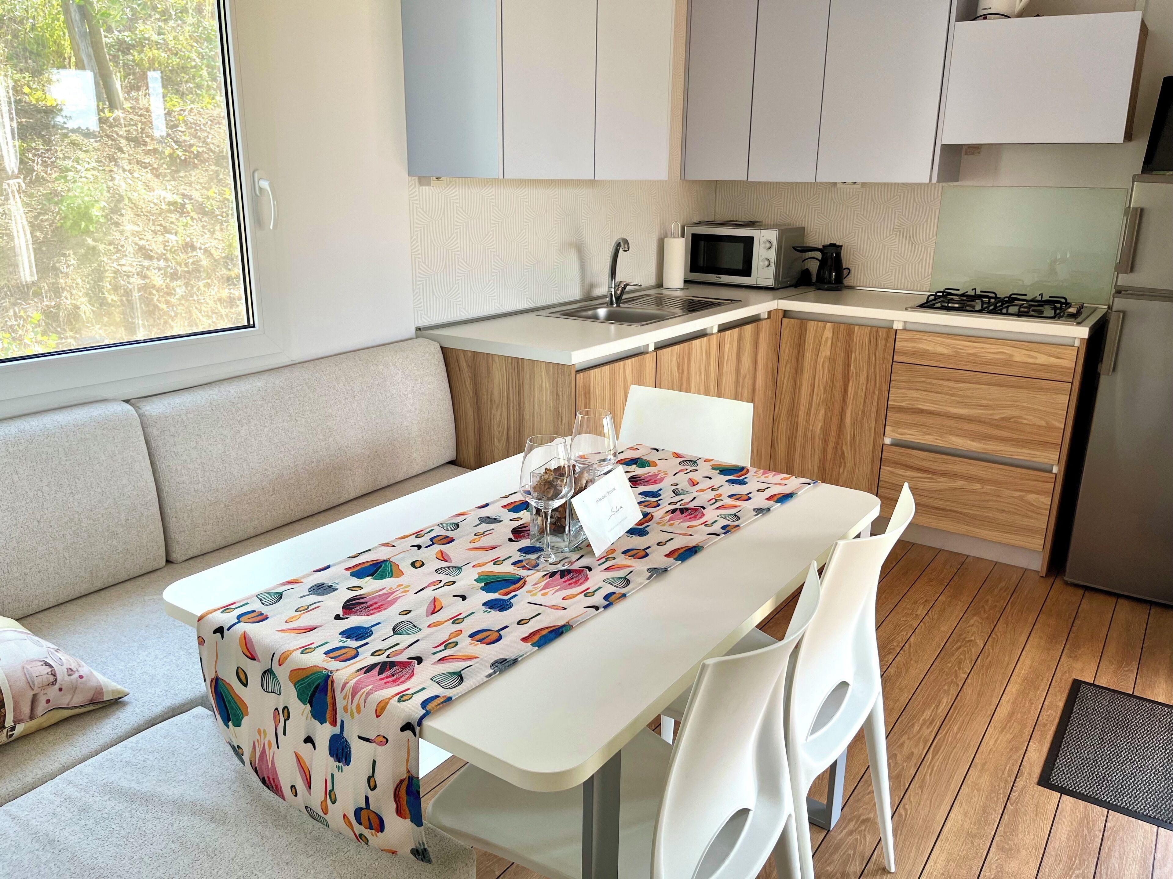 A modern kitchen with a dining area, featuring a table with a colorful tablecloth, white chairs, and a built-in microwave.