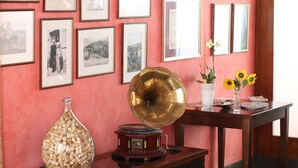 Une pièce avec un mur rose, des tableaux encadrés, un gramophone ancien, un vase rempli de bouchons de liège et une table sur laquelle est posé un vase de tournesols.