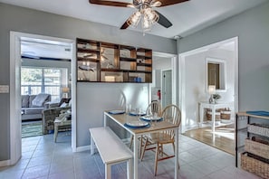 A dining area with a table set for four, a ceiling fan, and a view into the adjacent living room.