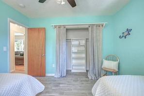 A bedroom with two beds, a wooden door, a closet with shelves, and a chair.