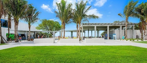 Un bâtiment moderne doté d’un espace extérieur couvert, de palmiers et d’une pelouse bien entretenue.