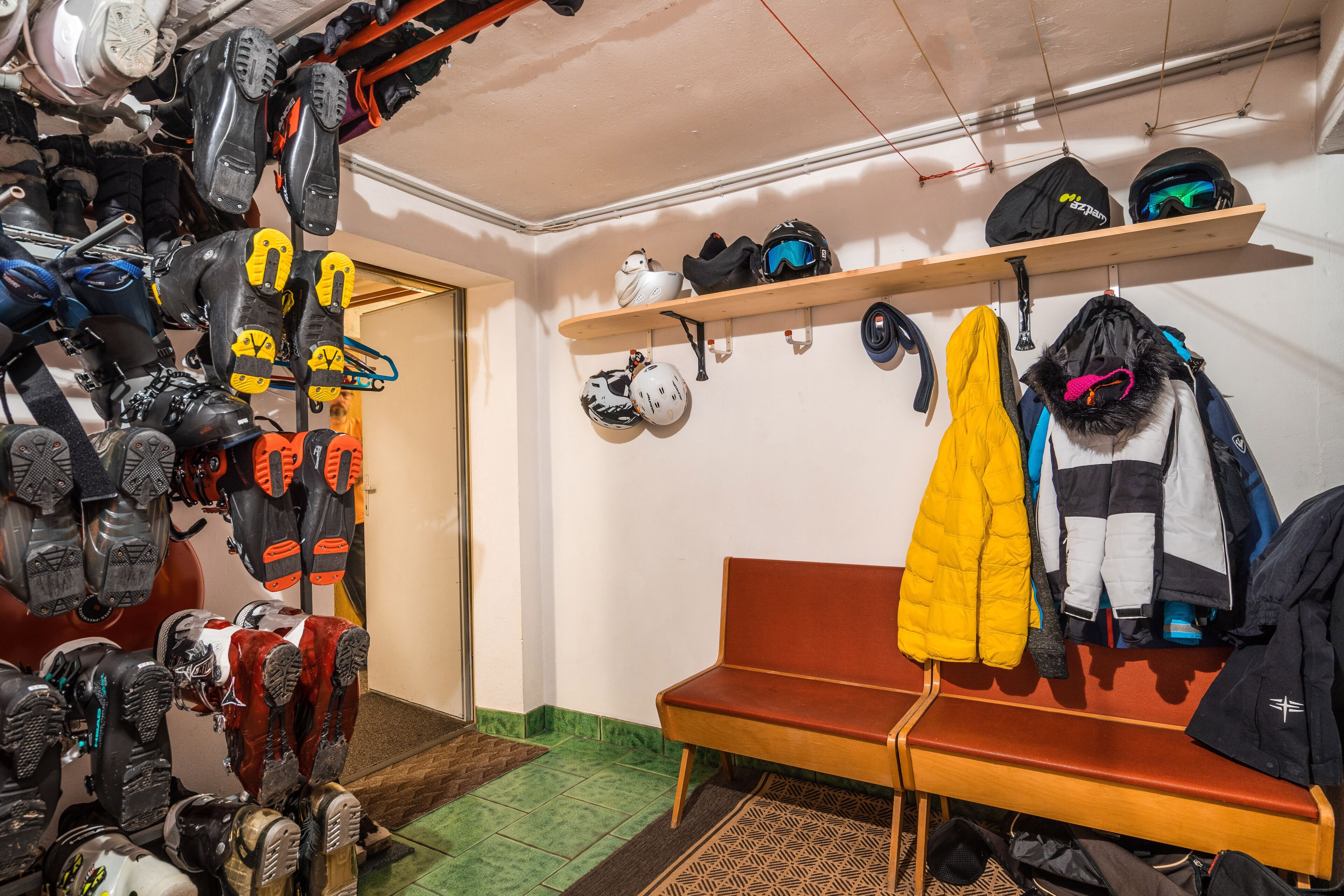 A room with a bench, helmets, and ski gear on shelves.