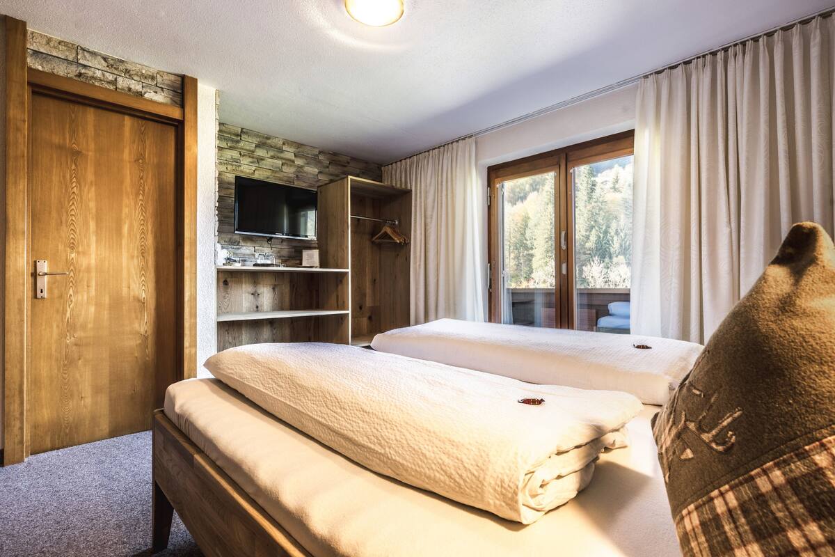 A hotel room with two beds, a wooden wardrobe, a television, and a window with curtains.