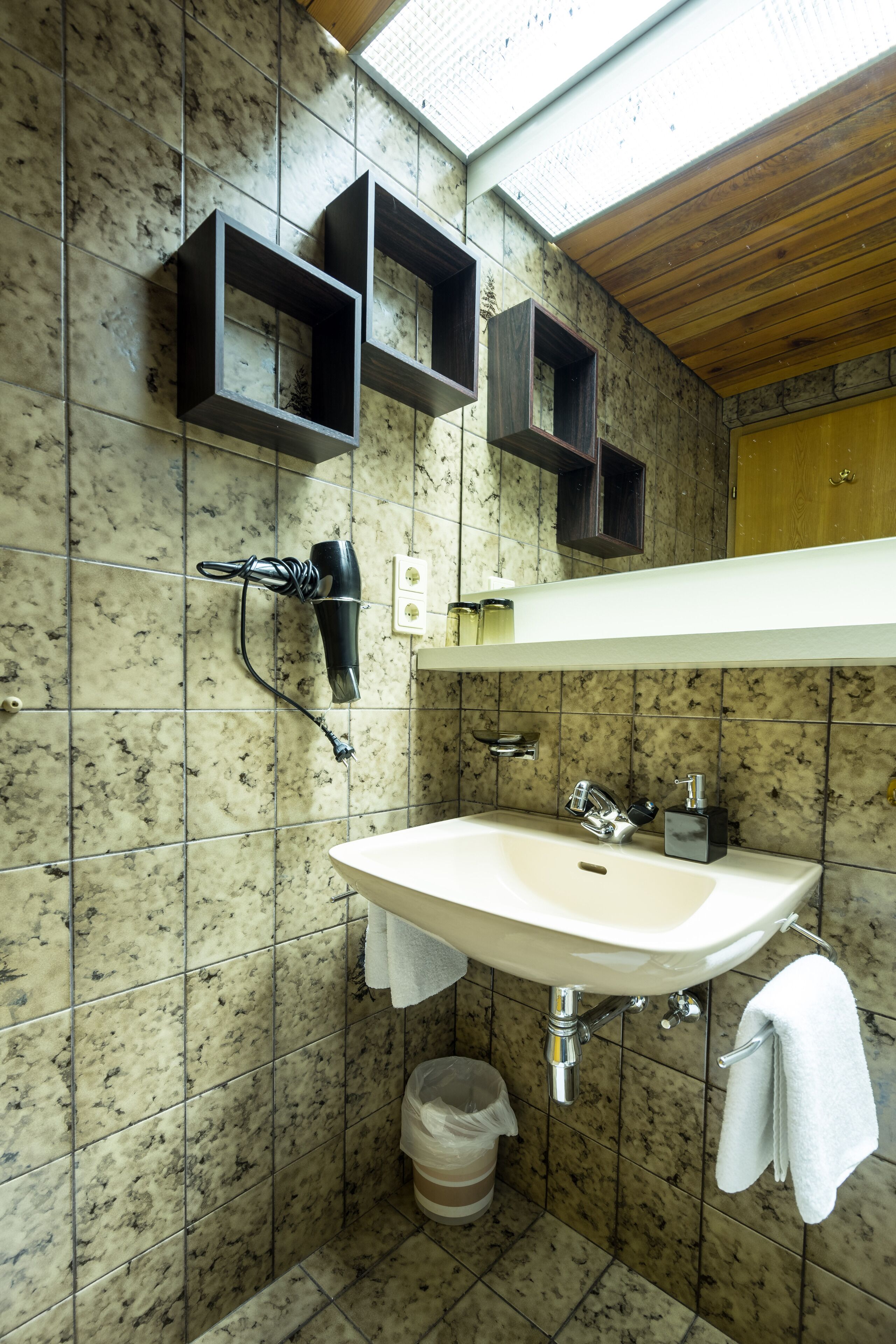 Une salle de bain avec un mur recouvert de carreaux de marbre, un lavabo blanc, un sèche-cheveux fixé au mur et un plafond en bois.