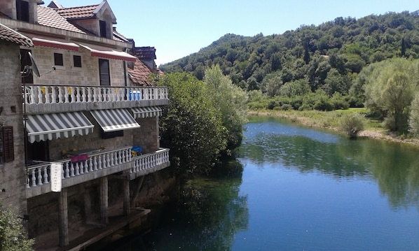 A building with a balcony overlooking a river, surrounded by greenery and hills. - Vacation home IDYLLE is located in the heart of the Skadar Lake National Park. (Cetinje)