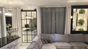 A modern living room with a grey sectional sofa, a glass coffee table, and a kitchen visible through a glass door. - Apartment Piękna4U 116 m2 (Śródmieście)