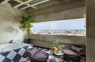 A balcony with a checkered floor, two wicker chairs, a small table with fruit, a potted plant, and a bathtub.