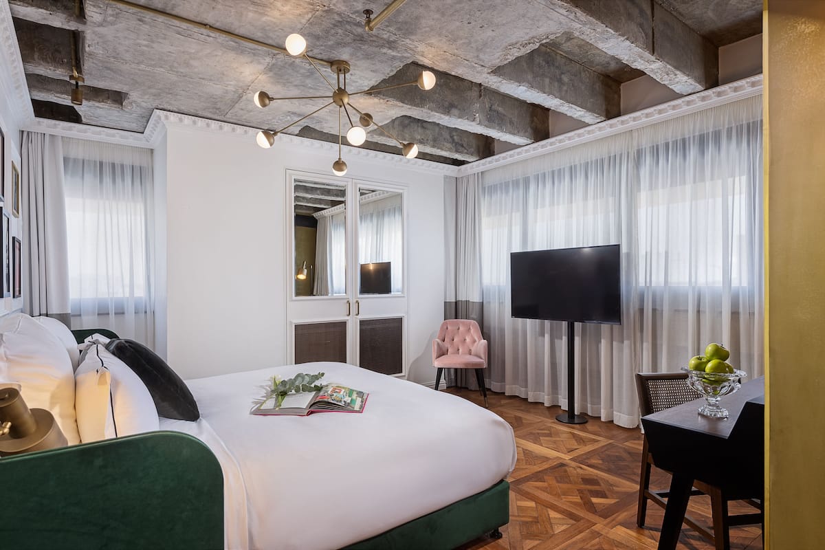 A hotel room with a large bed, a television, a dining table with a bowl of fruit, and a chair.