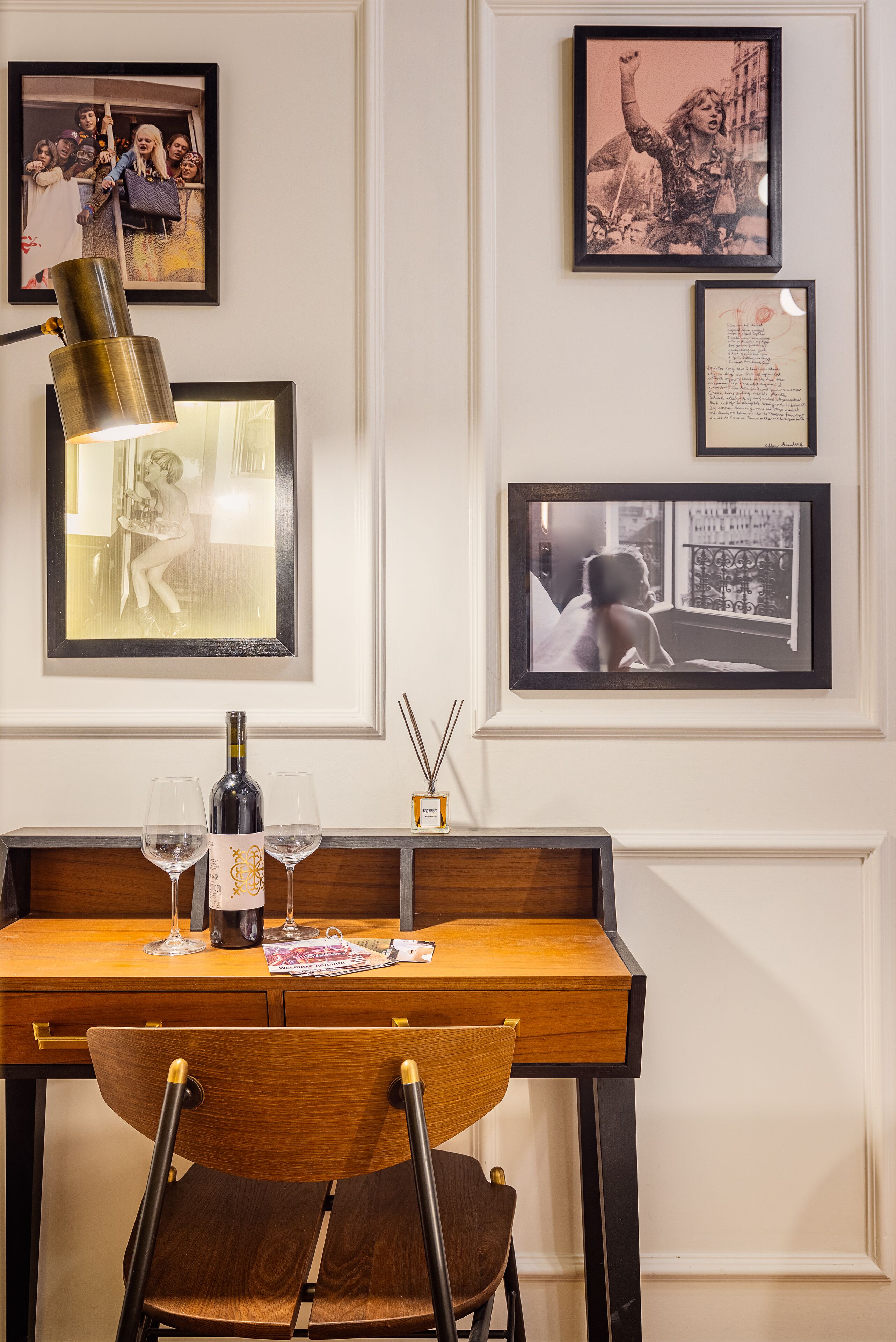 A wooden desk with two wine glasses, a bottle, and a framed picture of a woman.