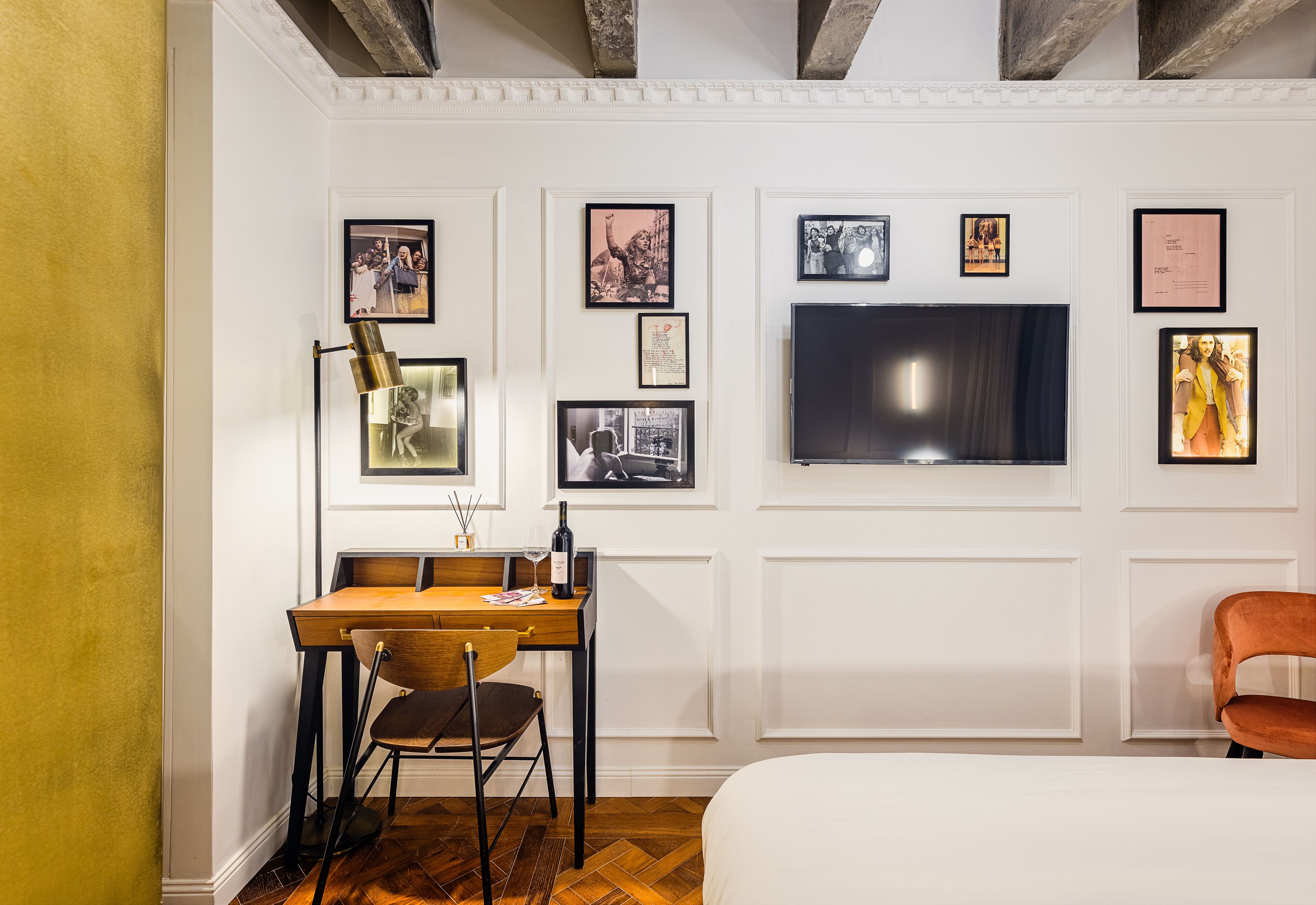 A hotel room with a wooden desk, a chair, a bed, and a TV mounted on the wall.