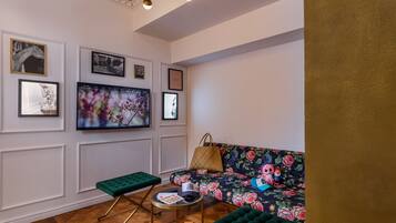 A room with a floral sofa, a green bench, and a small round table with a basket and a cup.