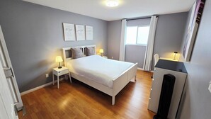 A bedroom with a bed, two bedside tables with lamps, a dresser, a window with curtains, and two wall art pieces. - Thien May Guest House. Up to 6 guests (Surrey)