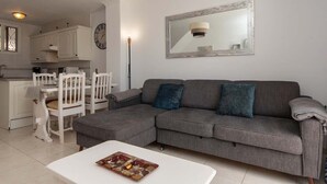 Un salon moderne avec un canapé gris, une table basse blanche et un coin repas comprenant des chaises blanches et une table blanche.