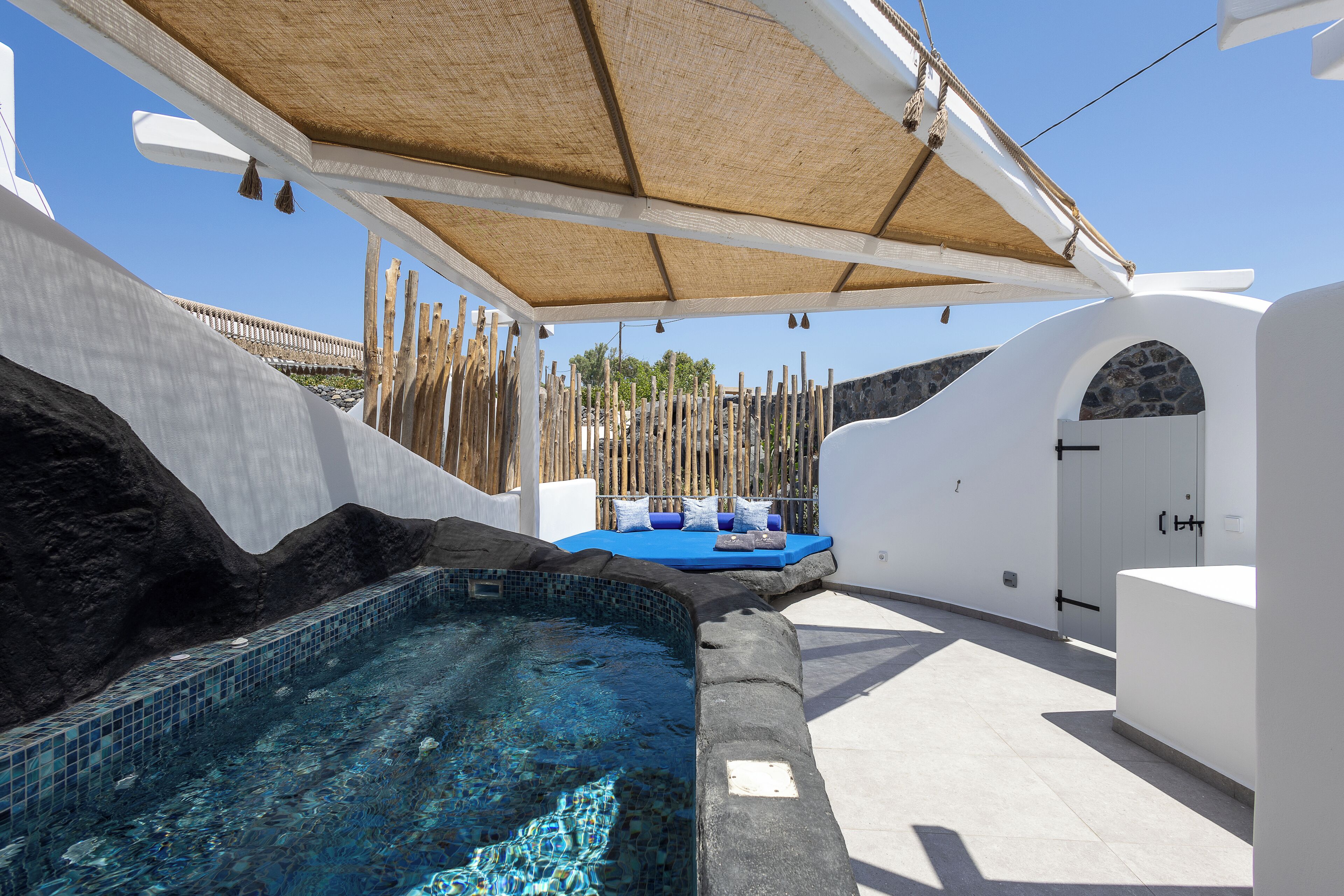 A pool area with a hot tub, a shaded seating area, and a stone wall.
