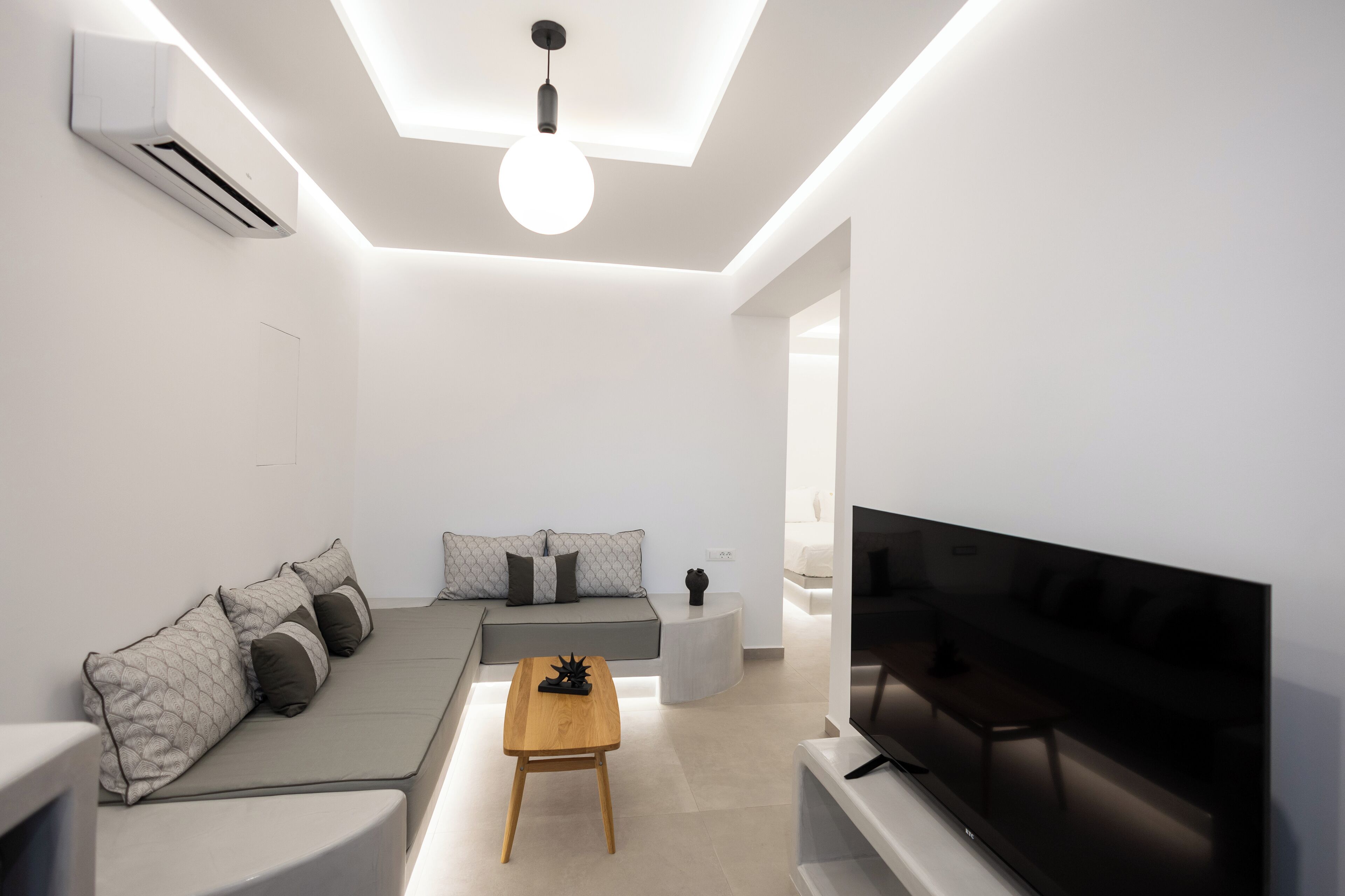 A modern living room with a sofa, a coffee table, a TV, and an air conditioning unit.