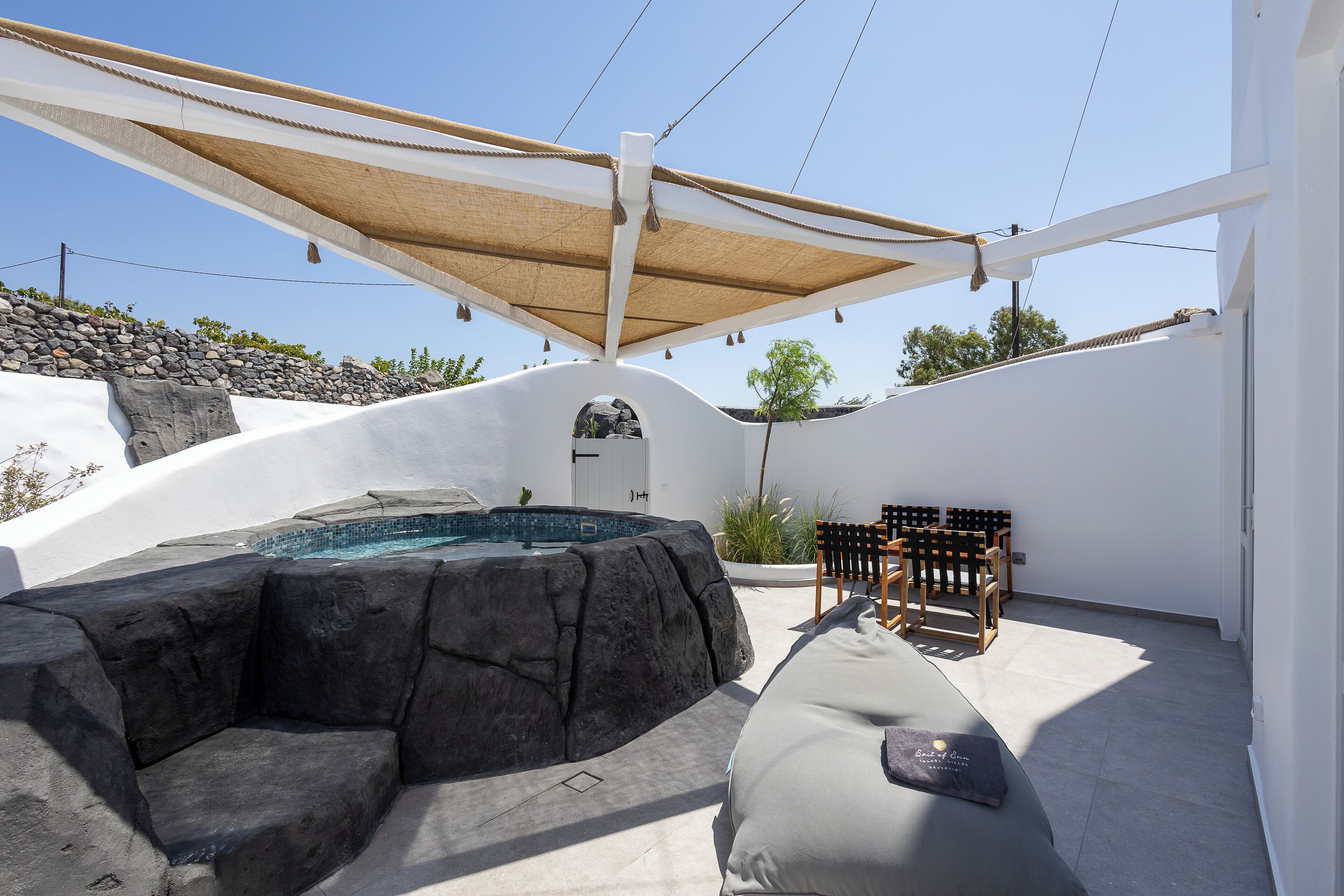 A modern outdoor pool area with a hot tub, a wooden bench, and a shaded seating area.