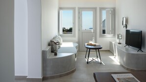Un salon moderne doté d’un espace salon aux lignes courbes, d’une petite table, d’un téléviseur et offrant une vue sur l’extérieur.