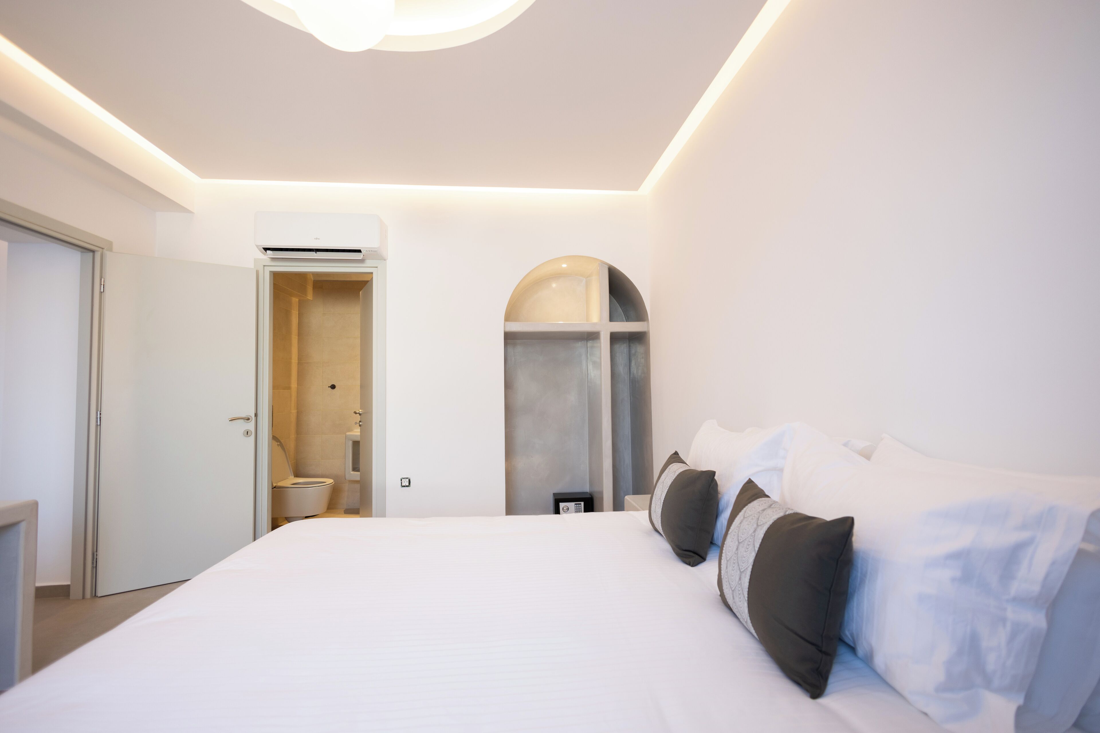 Ein modernes Hotelzimmer mit einem großen Bett, einem begehbaren Kleiderschrank und einem Badezimmer mit Dusche und Toilette.