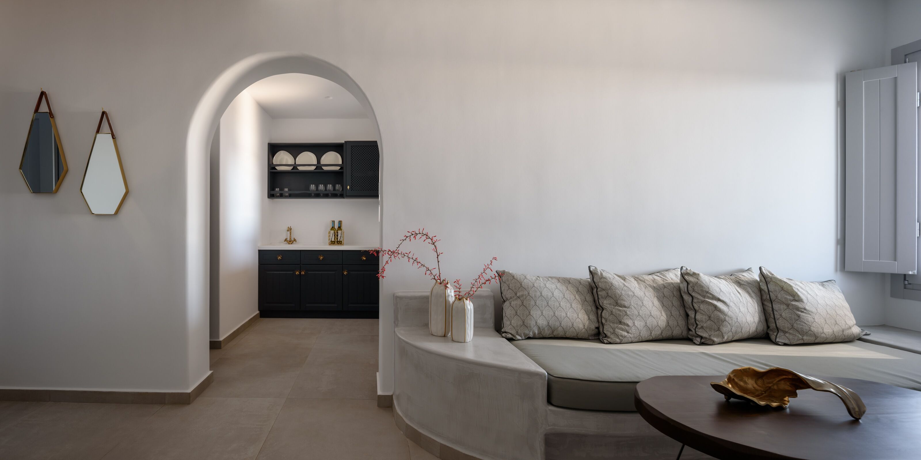 A modern living room with a curved sofa, a small round table, and a kitchen area with cabinets and a countertop.