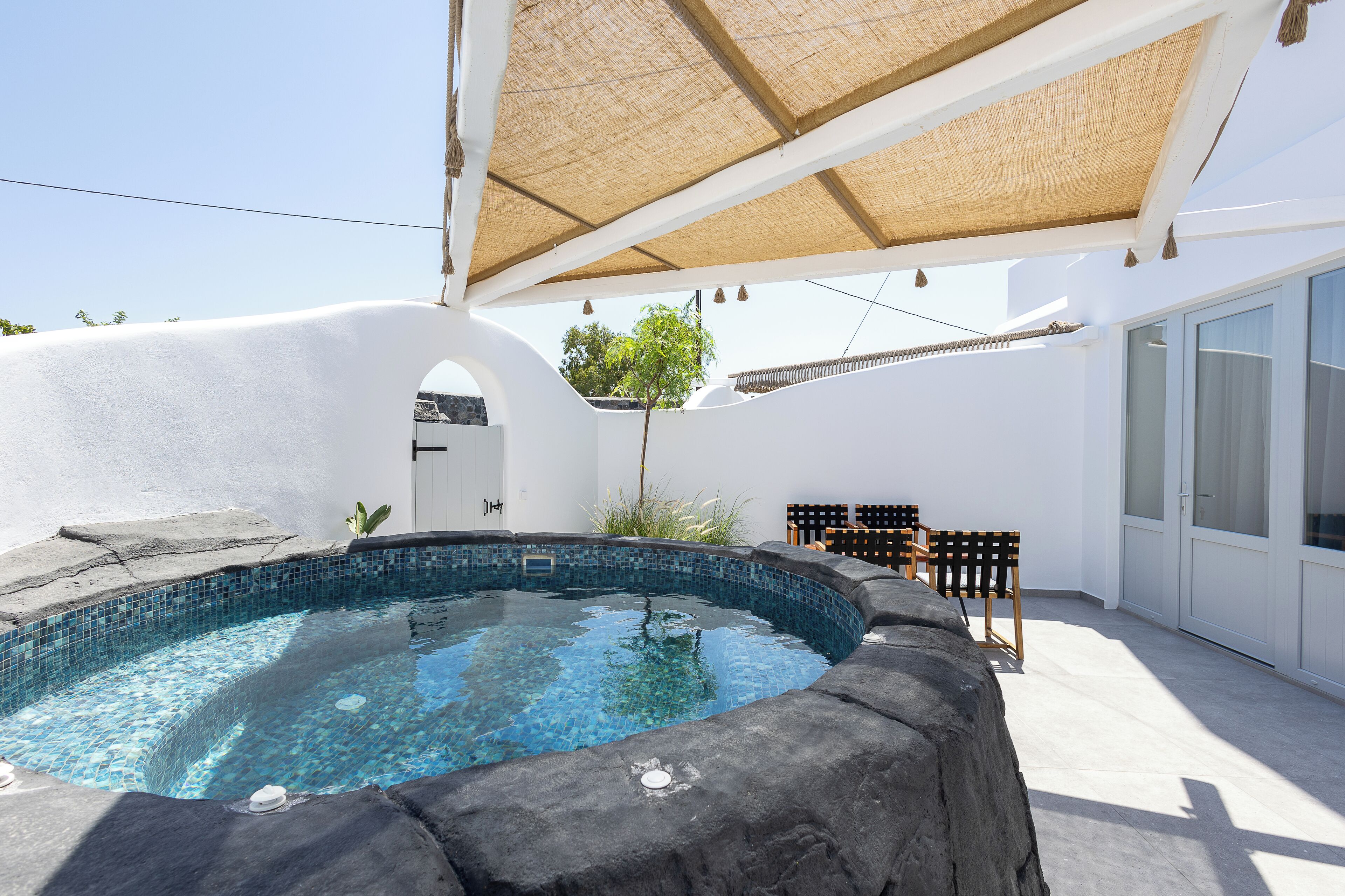 A swimming pool with a stone edge, surrounded by a white wall and a shaded area with a woven canopy.